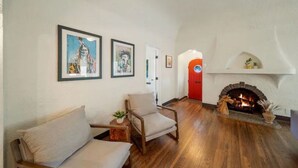 Ein Wohnzimmer mit Kamin, einer Couch und zwei gerahmten Kunstwerken an der Wand.