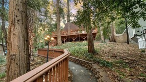 A wooden deck with a stone pathway leading to a building with a wooden structure and a balcony. - Cooled Micro Cabin | 1Bed + Loft (Crestline)