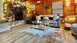 A cozy cabin interior with a stone fireplace, wooden walls, a sofa, and a coffee table. - Cooled Micro Cabin | 1Bed + Loft (Crestline)