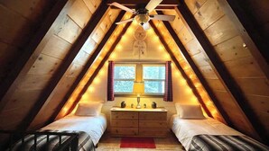 A cozy attic bedroom with two beds, a dresser, a window, and a ceiling fan. - Cooled Micro Cabin | 1Bed + Loft (Crestline)