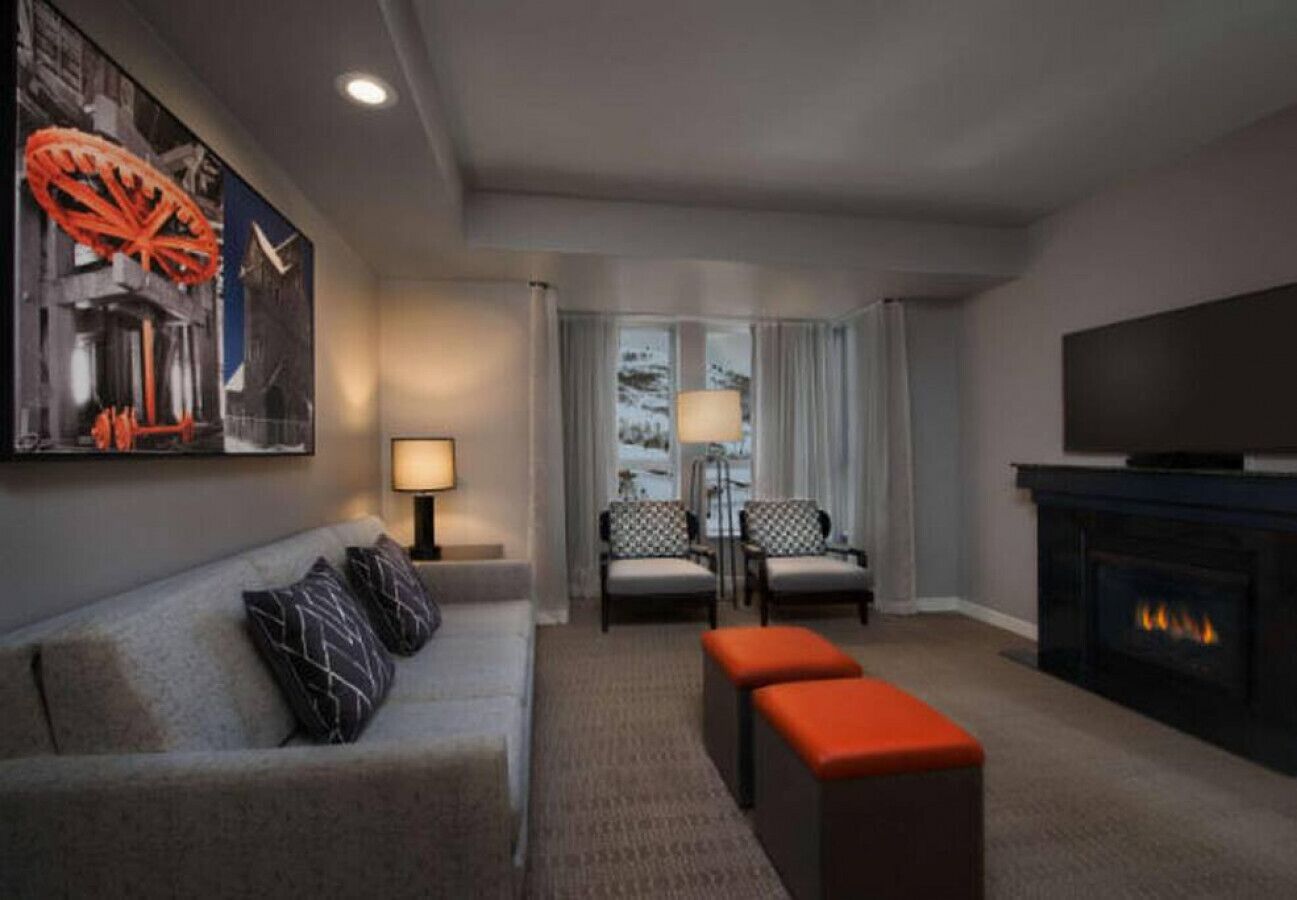 A modern living room with a sofa, ottoman, and chairs, a fireplace, and a television.