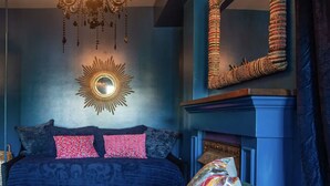 A room with a blue sofa, a round table, a chandelier, and a mirror. - "Shepherdess": Mystic Blue Salon With River View (Mystic)