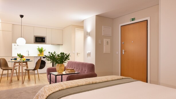 Hotelkamer met een bed, een zithoek met een tafel en stoelen, een kitchenette en een deur met een vluchtwijzer.