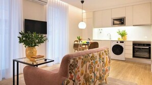Een modern appartement met een zithoek, inclusief een bank en salontafel, een eethoek met tafel en stoelen, en een keuken met apparatuur.