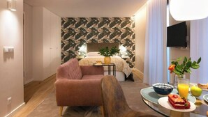 Een moderne hotelkamer met een bed, een roze fauteuil, een ontbijttafel en een televisie.