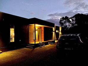 A modern house with a large glass door, a visible interior, and a parked car in front.