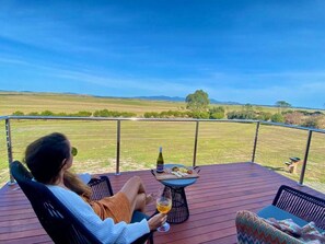 A person relaxing on a deck with a table and chairs, overlooking a grassy field. - Wamoon Retreat - The Apartment ~ Luxury Gateway to Wilsons Prom (Yanakie)