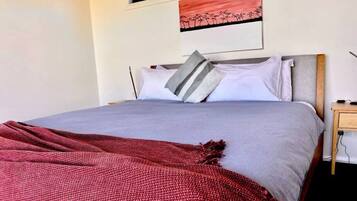 A bed with a grey and white bedding, a red blanket, and a wooden nightstand with a lamp.