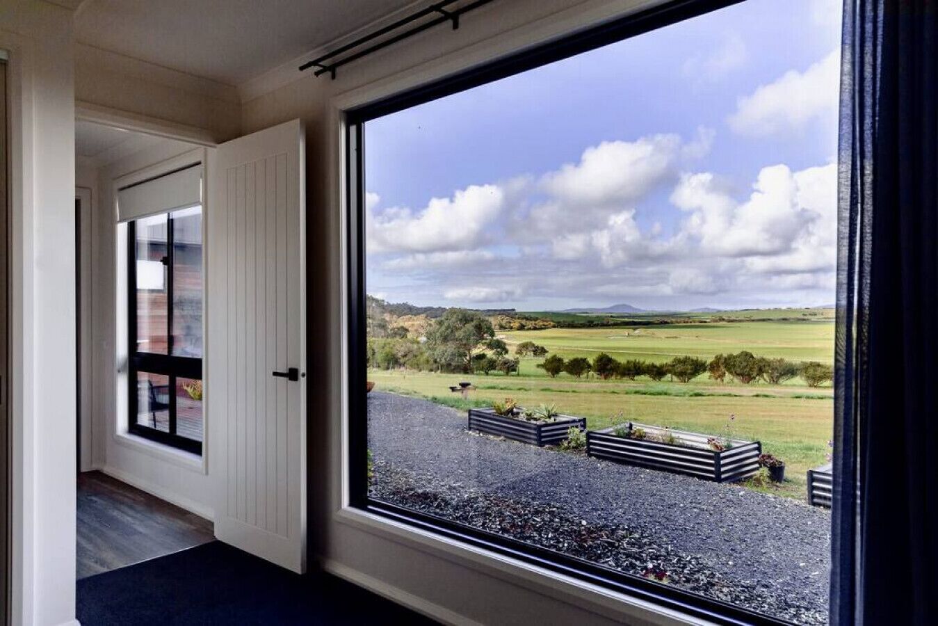 A room with a large window offering a view of a rural landscape with fields and trees.