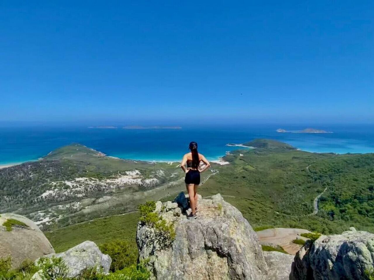 Une personne se tient debout sur un promontoire rocheux, d’où elle domine un paysage côtier.