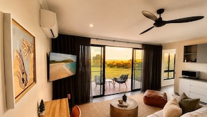 A modern living room with a flat-screen TV, a ceiling fan, a dining area, and a large sliding glass door leading to an outdoor patio. - Wamoon Retreat - The Apartment ~ Luxury Gateway to Wilsons Prom (Yanakie)
