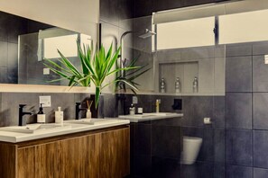 A modern bathroom with two sinks, a mirror, and a shower.