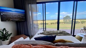 A bedroom with a large bed, a television on the wall, and a view of the countryside. - Wamoon Retreat - The Apartment ~ Luxury Gateway to Wilsons Prom (Yanakie)