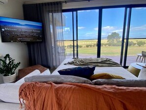 A modern bedroom with a large bed, a TV on the wall, and a view of the countryside.