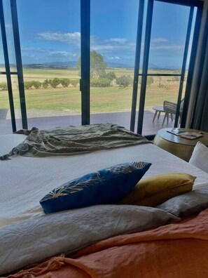 A bedroom with a large window, a bed with pillows, and a view of a grassy field. - Wamoon Retreat - The Apartment ~ Luxury Gateway to Wilsons Prom (Yanakie)
