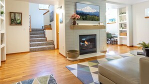 A modern living room with a fireplace, a staircase, and a view of a mountain.