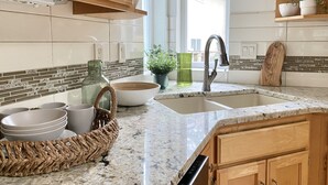 A kitchen with wooden cabinets, a granite countertop, a sink, and a window with a view of a house.