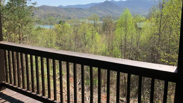 A view from a balcony with a wooden railing, overlooking a forested valley and distant mountains. - Cute cabin😊Pretty Views! Clean! ONLY 1 MILE TO TOWN! (Hiawassee)