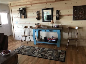 Ein Holzinterieur mit einem blauen Tisch, zwei Stühlen, einem Teppich und Wanddekorationen, darunter ein Spiegel und Geweihe.