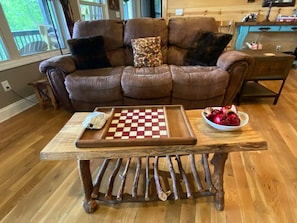 Ein gemütliches Wohnzimmer mit einem braunen Ledersofa, einem Couchtisch mit Schachbrettmuster und einer Obstschale.