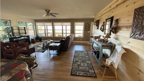 A spacious living room with a wooden floor, a ceiling fan, a large window, and a fireplace. - Cute cabin😊Pretty Views! Clean! ONLY 1 MILE TO TOWN! (Hiawassee)