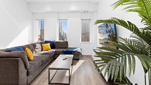 A modern living room with a sectional sofa, a coffee table, and large windows offering city views.