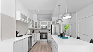A modern kitchen with white cabinetry, stainless steel appliances, and pendant lighting.