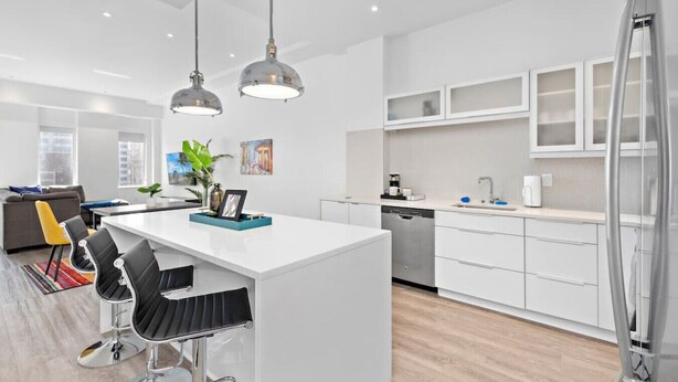 A modern kitchen with white cabinetry, a central island with bar stools, pendant lighting, and a dishwasher.