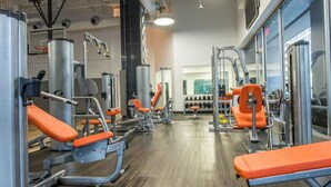 Un gimnasio con diferentes máquinas de ejercicio, estantes para pesas y bancos naranjas.