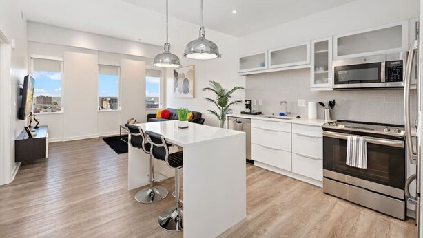 Una cocina moderna con armarios blancos, electrodomésticos de acero inoxidable y una isla central con taburetes de bar.