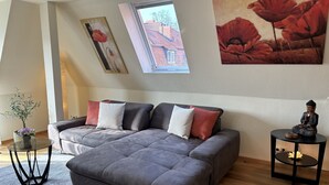 Ein modernes Wohnzimmer mit einem grauen Ecksofa, einem kleinen runden Tisch und einer Buddha-Statue.