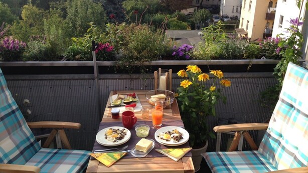 Ein Balkon mit Frühstückstisch und Stühlen, mit Blick auf einen Garten und Gebäude.