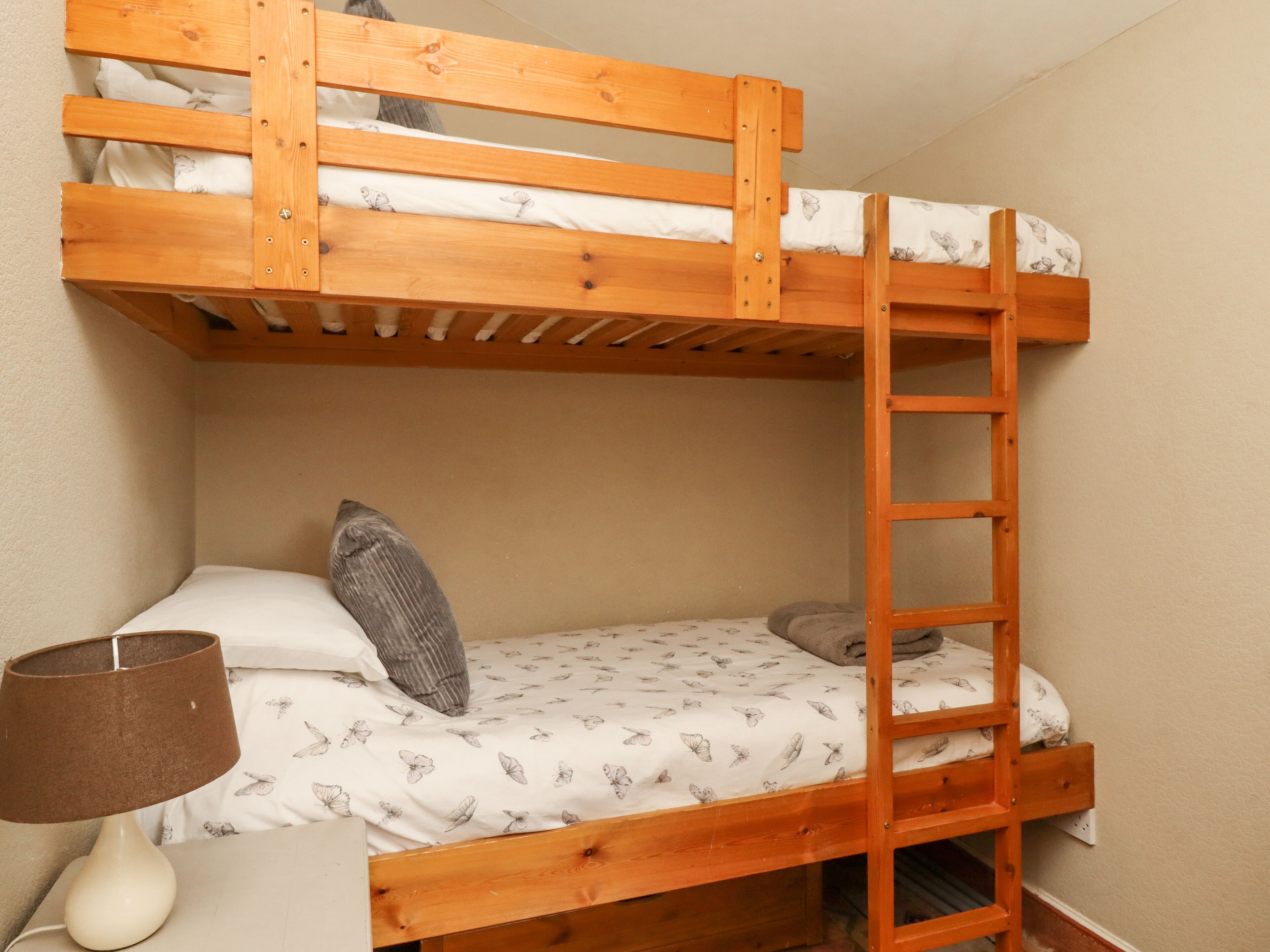 A bunk bed with a ladder, a pillow, and a lamp on a bedside table.