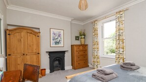 A bedroom with a bed, wooden wardrobe, dresser, fireplace, and a window with curtains. - 3 Hamilton Terrace (Harrogate)