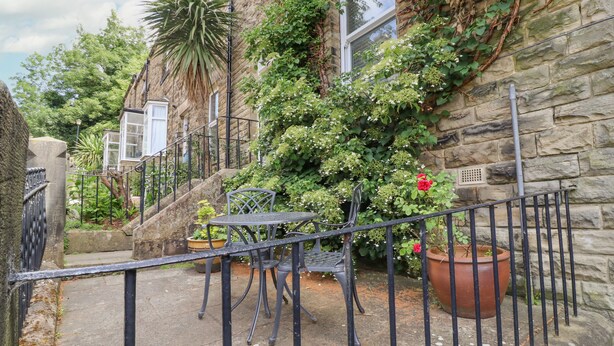 A stone building with a staircase leading to a balcony. There are potted plants and a metal table with chairs on the balcony. - 3 Hamilton Terrace (Harrogate)