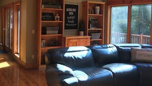 Interior acogedor de una cabaña con techo de madera, estanterías empotradas, un sofá de cuero y ventanas amplias que ofrecen vistas al exterior.