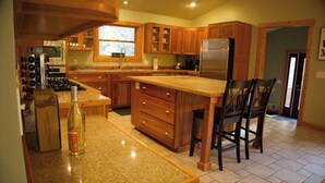 Una cocina con armarios de madera, un refrigerador de acero inoxidable, encimera de granito y una botella de vino.