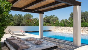 Un espace aménagé au bord de la piscine, avec une pergola en bois, des chaises longues et un mur en pierre.