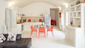 Une cuisine moderne avec des meubles blancs, un coin repas avec des chaises orange et un canapé rouge.