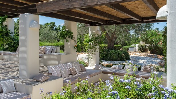 Un espace extérieur aménagé avec une pergola, des bancs rembourrés et un jardin en arrière-plan.