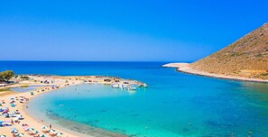 Ein Küstenstrand mit klarem türkisblauem Wasser, einem Sandufer und mehreren Booten, die in der Nähe liegen.
