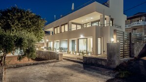 A modern two-story house with a balcony, a driveway, and a tree in the foreground. - Aelia - Vacation house with private pool in Kounoupidiana, Crete (Kounoupidianá)