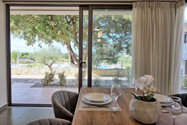 A dining area with a table set for two, a view of a pool and trees outside, and a sliding glass door.