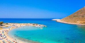 Ein Küstenstrand mit klarem türkisblauem Wasser, einem Sandstrand und Booten in der Nähe, die vor Anker liegen.