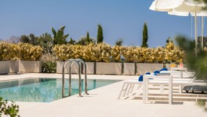 A pool area with a clear blue sky, a pool, lounge chairs, and a white umbrella. - Dioni - Vacation house with private pool in Kounoupidiana, Crete (Plakoúres)