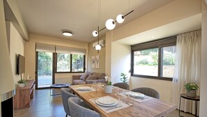 A modern dining area with a wooden table set for four, grey chairs, and a sofa in the background. - Dioni - Vacation house with private pool in Kounoupidiana, Crete (Plakoúres)
