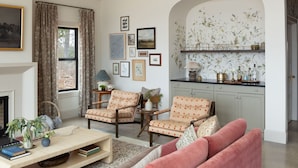 A living room with a fireplace, two armchairs, a sofa, a coffee table, and a kitchen area with a countertop and cabinets. - The Lark Haus: Luxury Home with stunning lake view (Elizabeth)