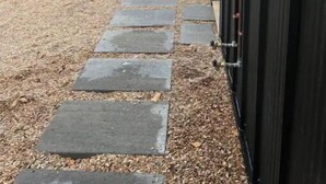 A stone pathway leading to a building with a black exterior, surrounded by trees and a clear sky. - The Lark Haus: Luxury Home with stunning lake view (Elizabeth)