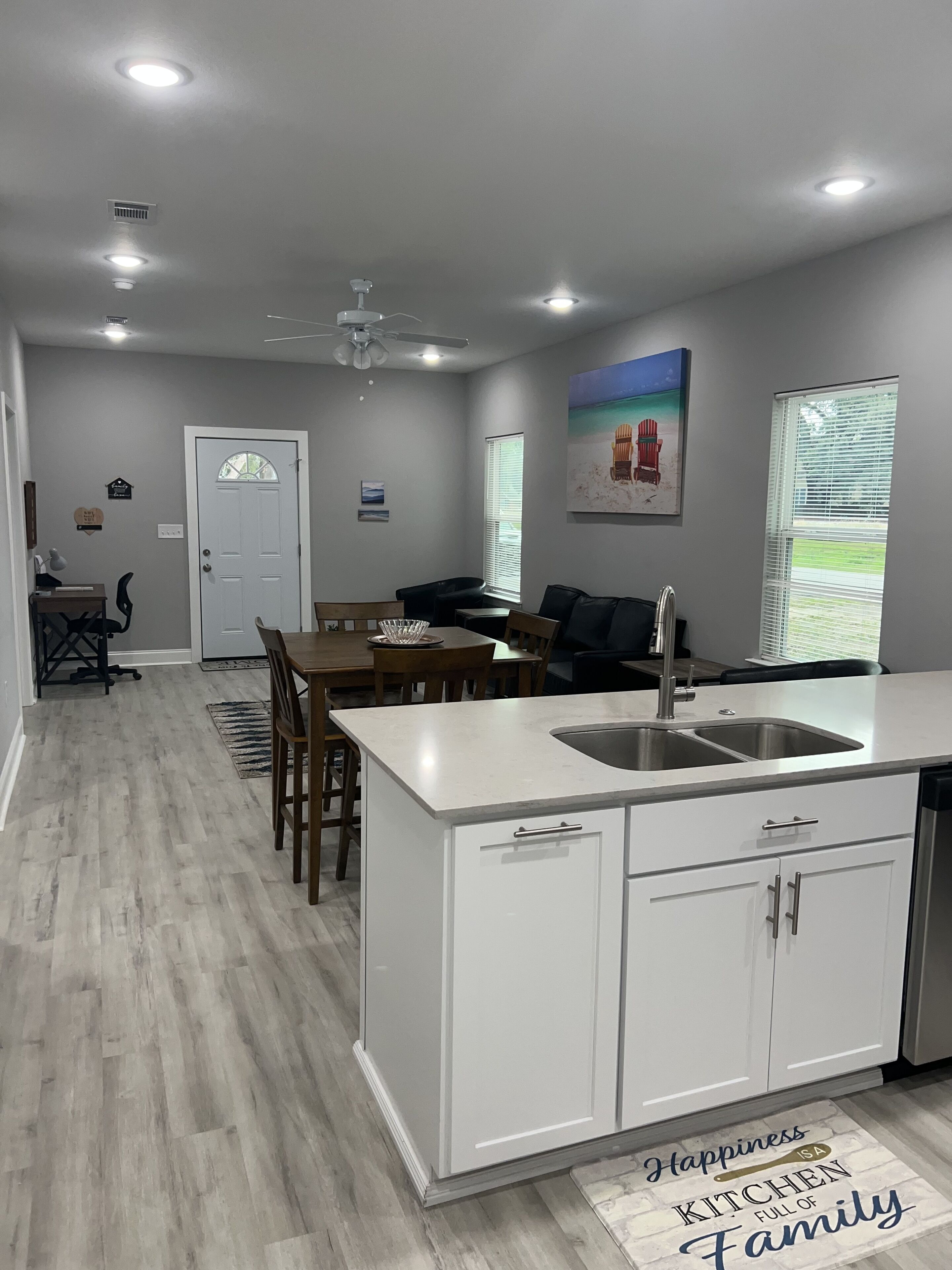 Cocina moderna con armarios blancos, una isla central con pileta y un comedor con sillas y mesa de madera.