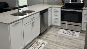 A modern kitchen with white cabinets, stainless steel appliances, and a wooden floor.
